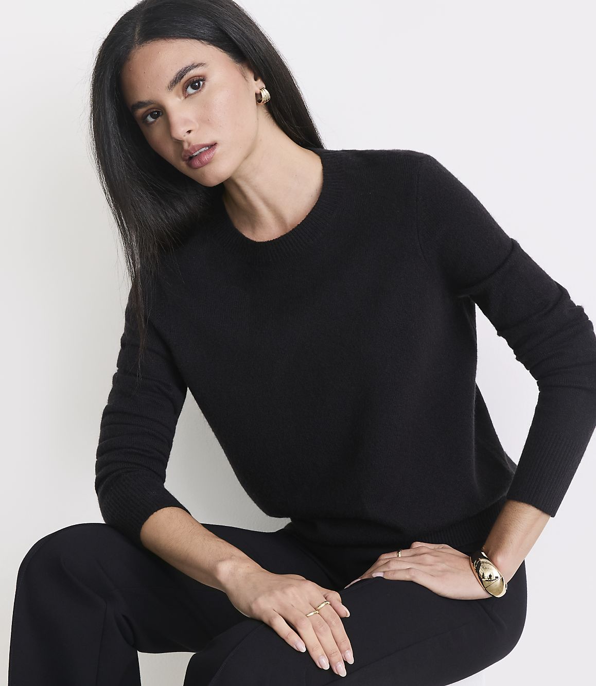 A woman in a black sweater and pants poses against a plain white background.
