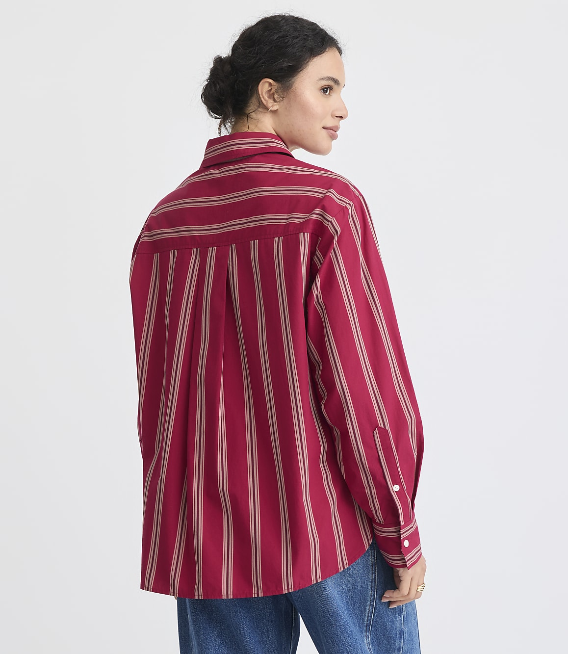 A woman in a red striped shirt and tan pleated skirt stands against a plain white background.