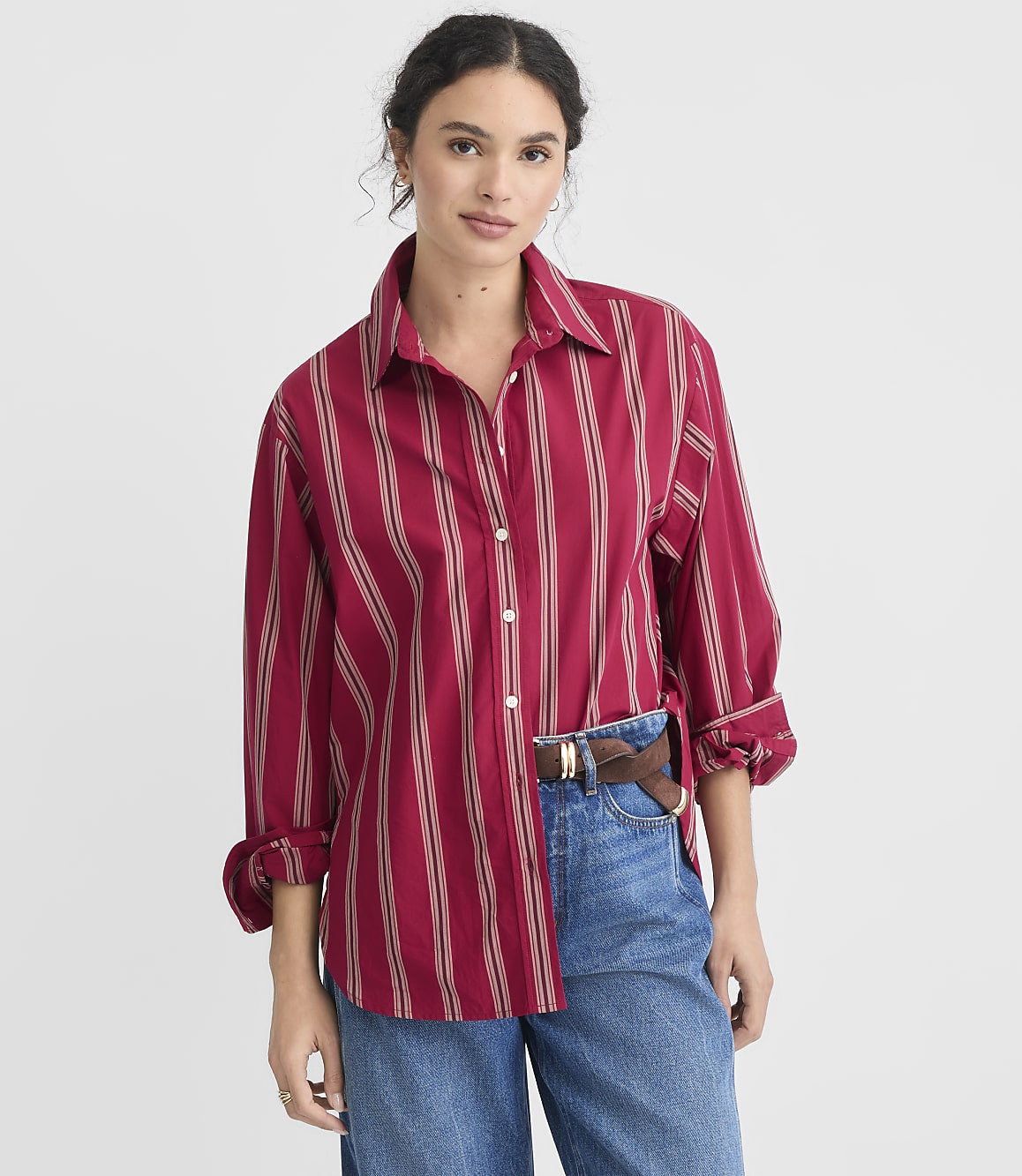 A woman in a red striped shirt and tan pleated skirt stands against a plain white background.