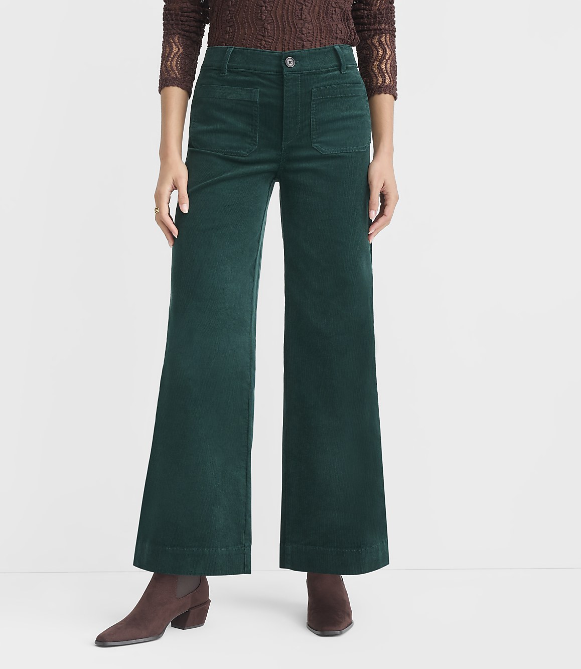 A person stands in the foreground wearing wide-leg green corduroy pants and brown boots, against a plain white background.