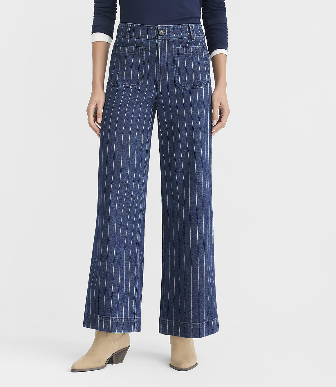 A person stands in wide-leg pinstripe jeans and black flats against a plain white background.