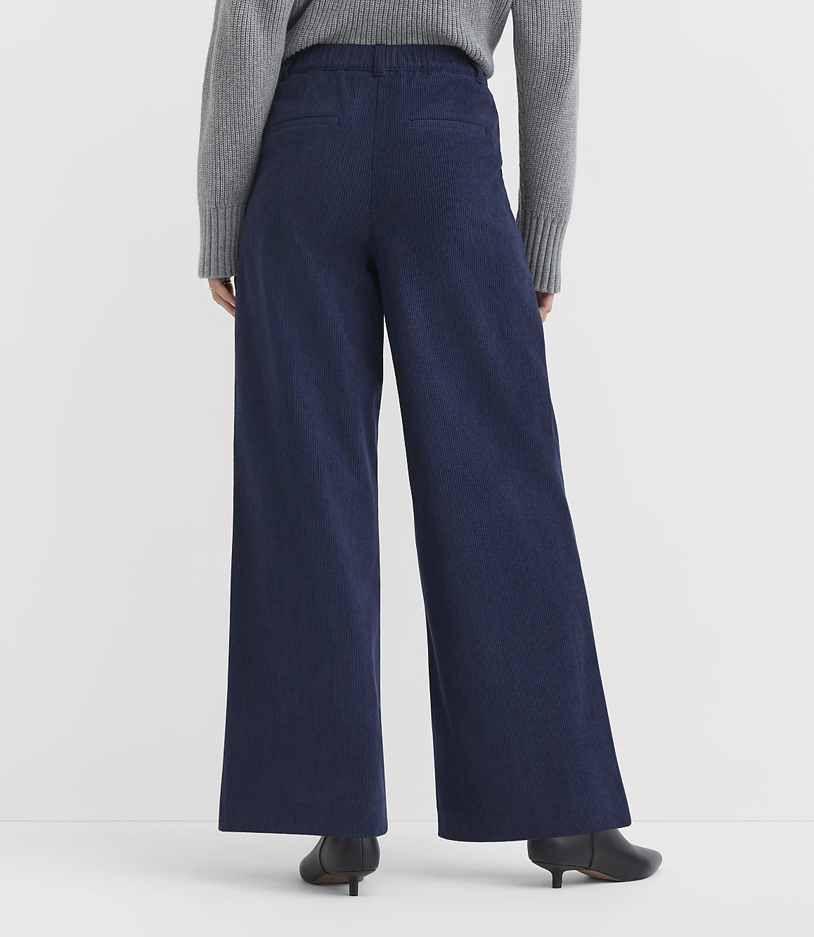 A person wearing wide-leg navy pants and a grey sweater stands against a plain white background.