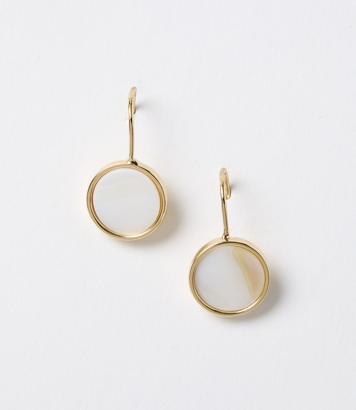 A pair of gold-rimmed circular mother-of-pearl earrings hang against a plain white background.