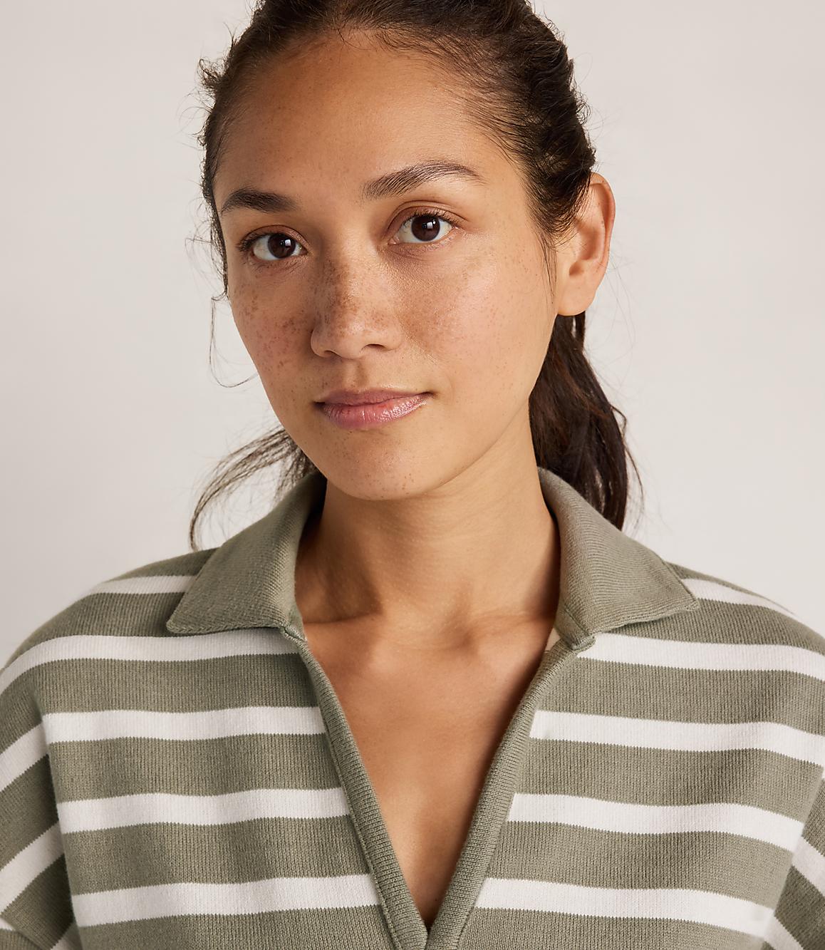 A woman with freckles and dark hair pulled back wears a green and white striped collared shirt against a plain, light background.