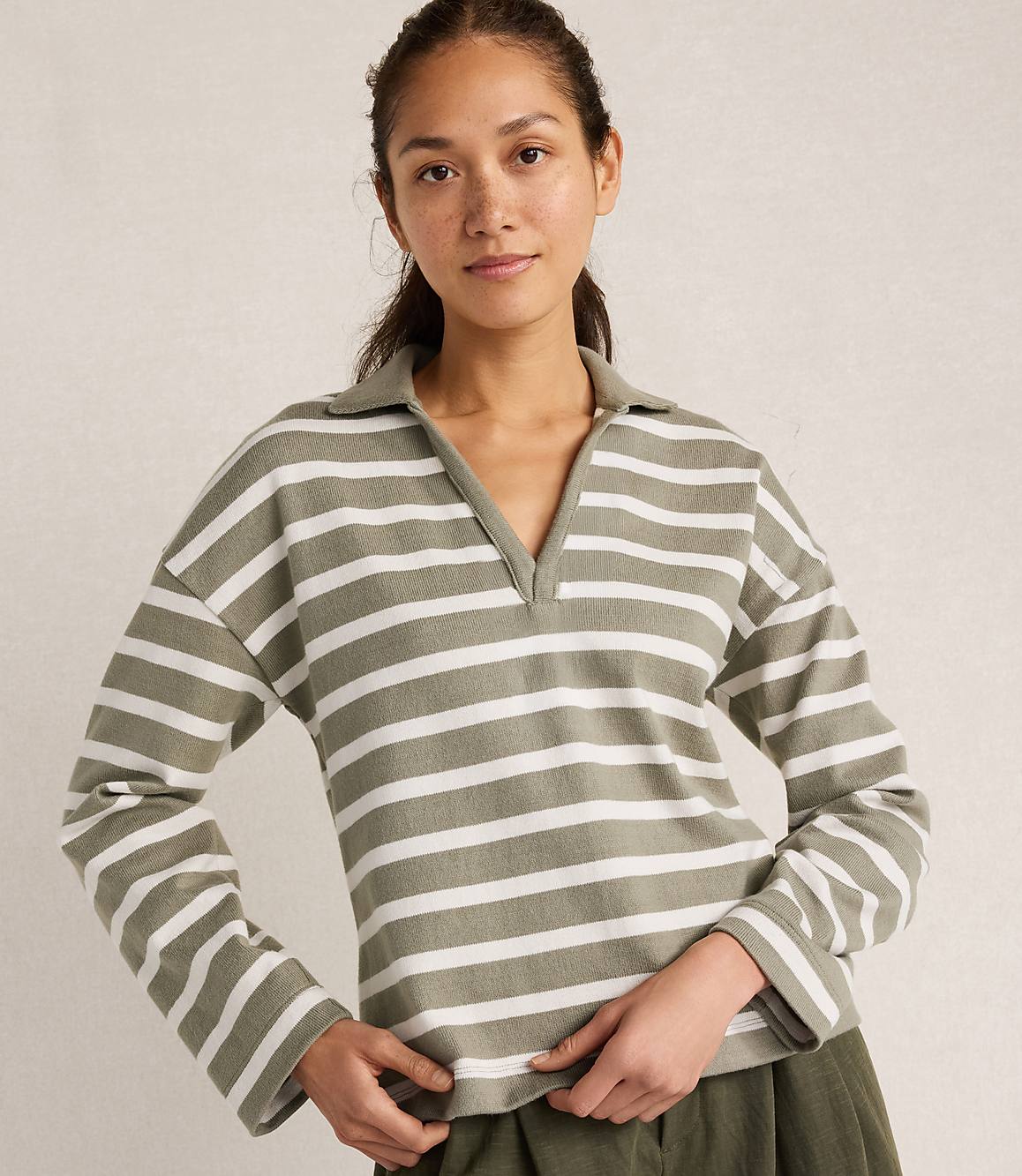 A woman in a striped shirt stands against a plain, light-colored background.