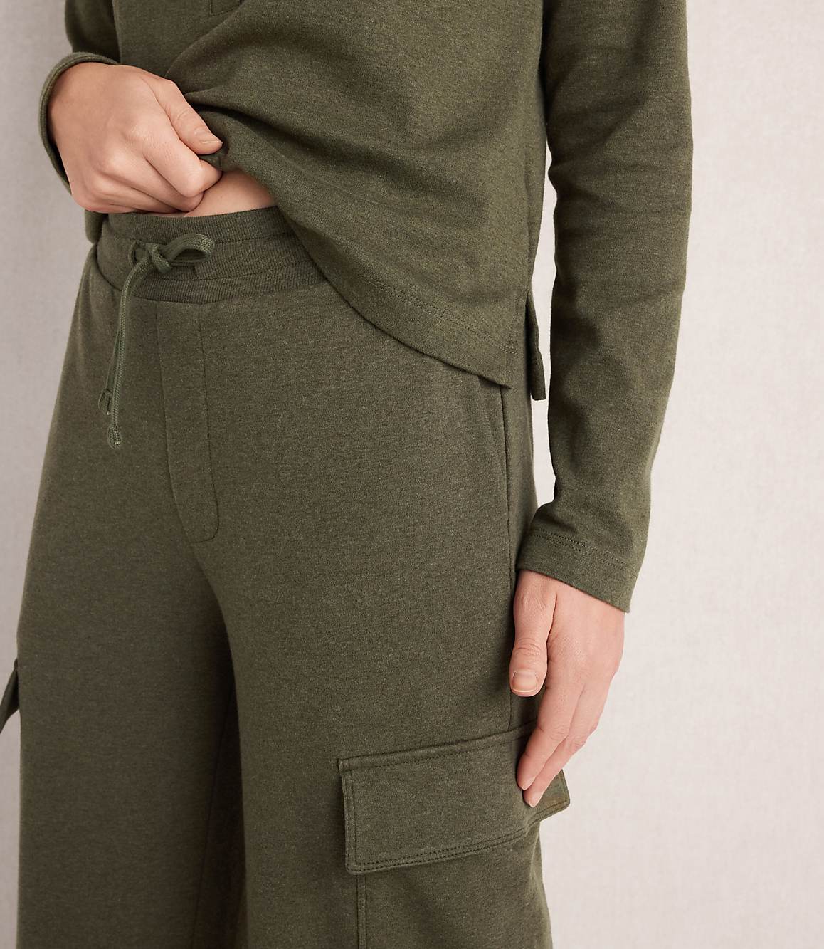 A person in a green loungewear set with cargo pockets stands against a textured, light-colored wall.