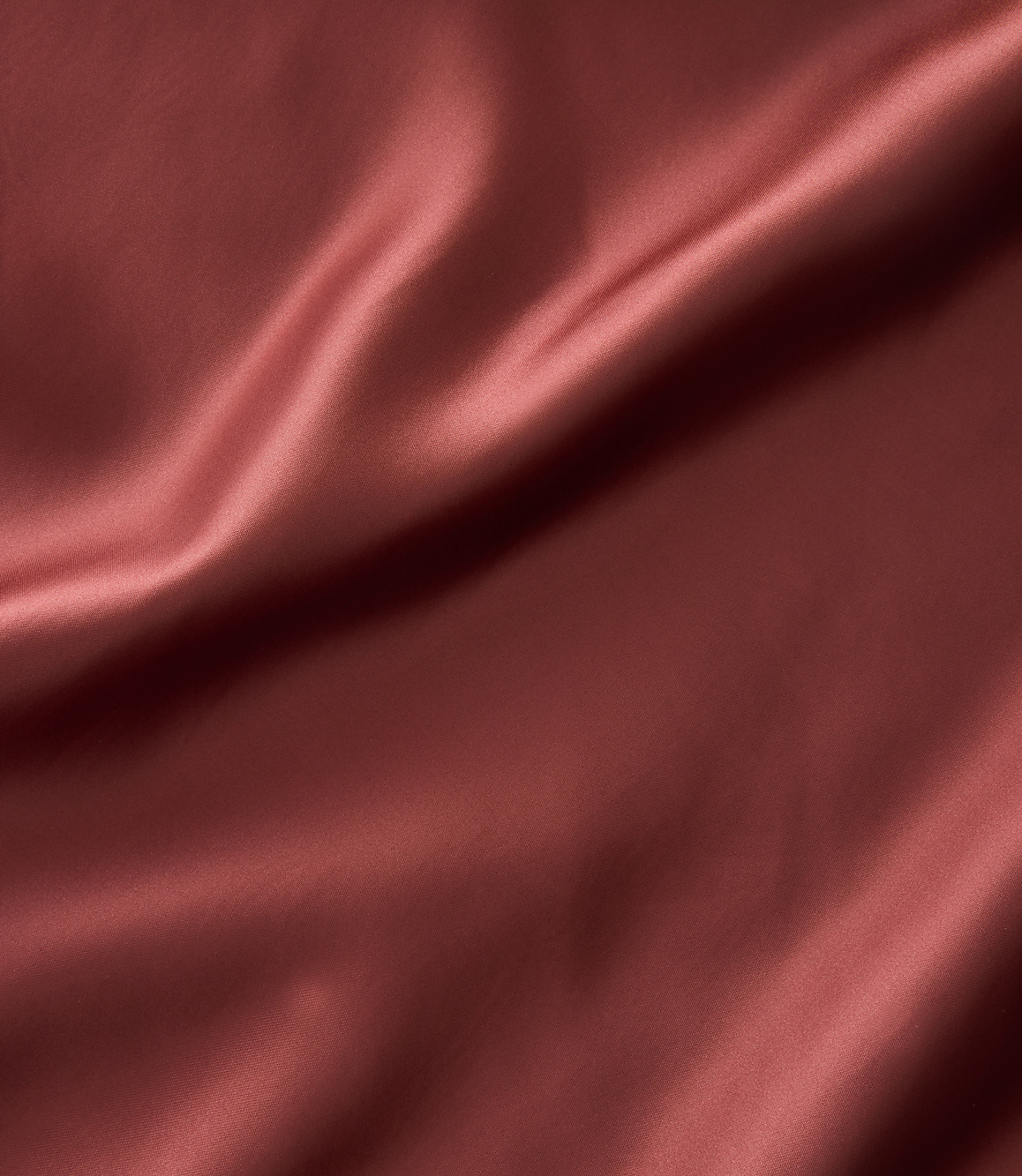 A close-up of rust-colored satin fabric with soft folds and highlights fills the frame.