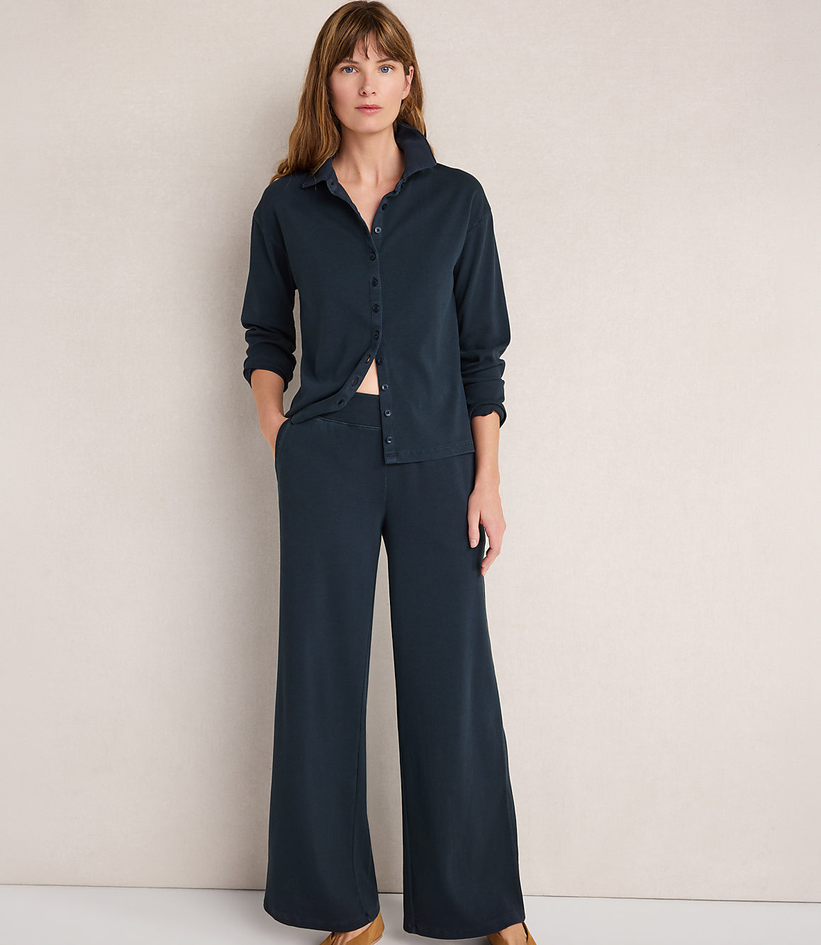 A woman in a dark blue pajama set stands against a plain, light-colored wall.