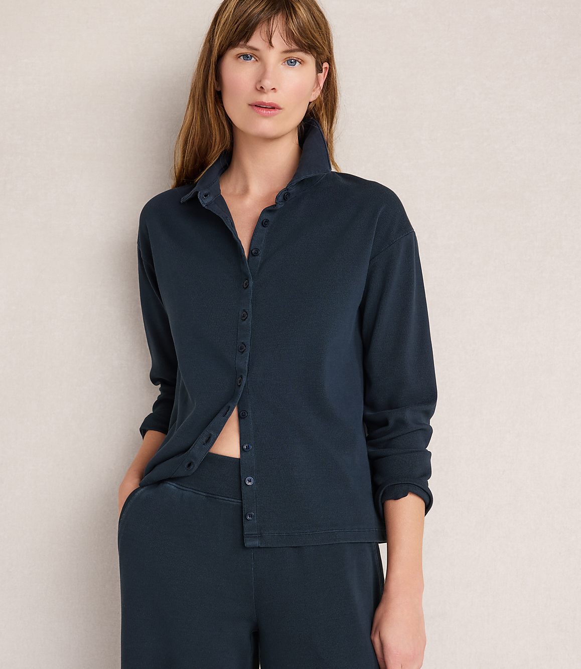 A woman in a dark blue ribbed shirt and pants stands against a plain, light-colored background.