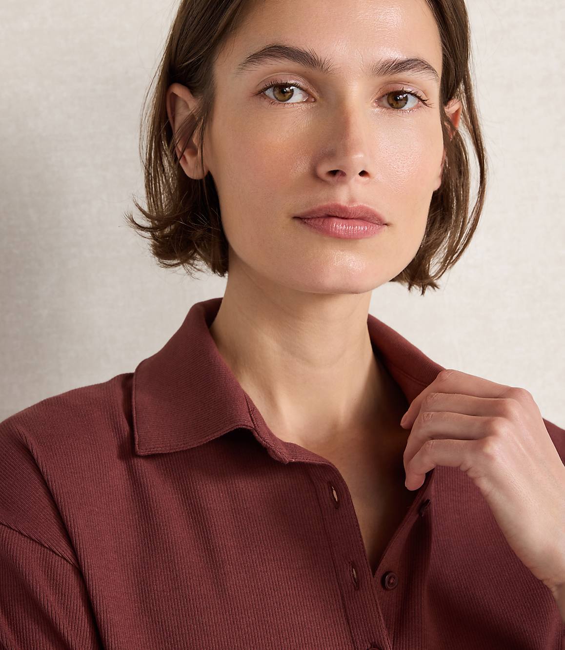 A woman with short brown hair and a maroon collared shirt is shown in the foreground, with a textured beige background behind her.