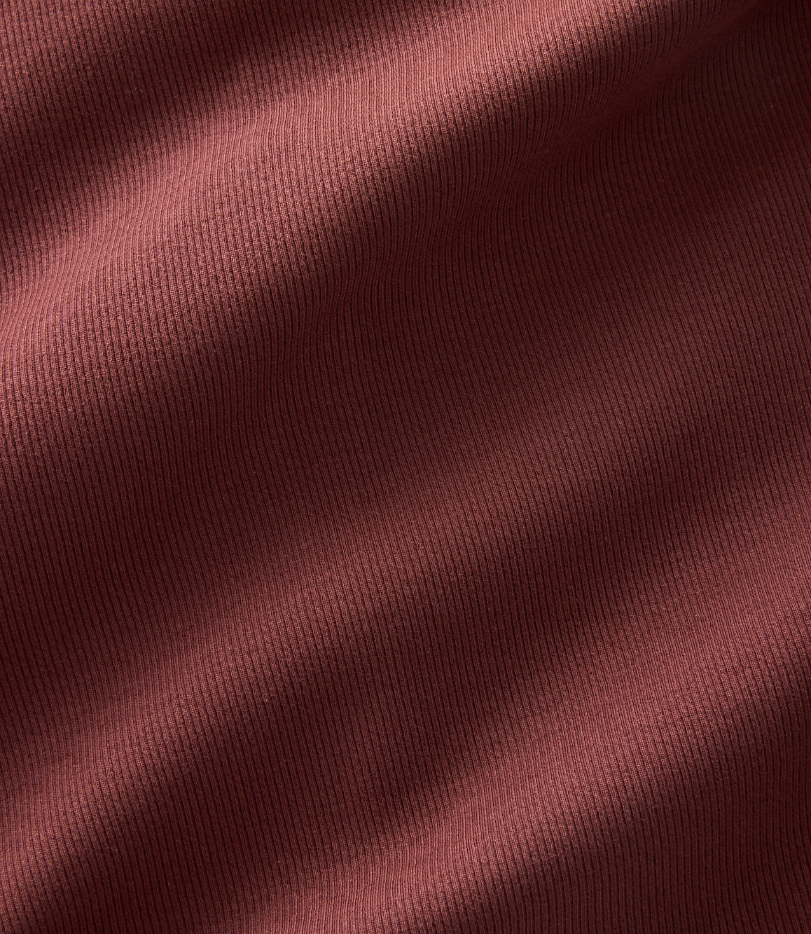 A close-up view of a textured, reddish-brown fabric fills the frame, with subtle folds and shadows creating depth.