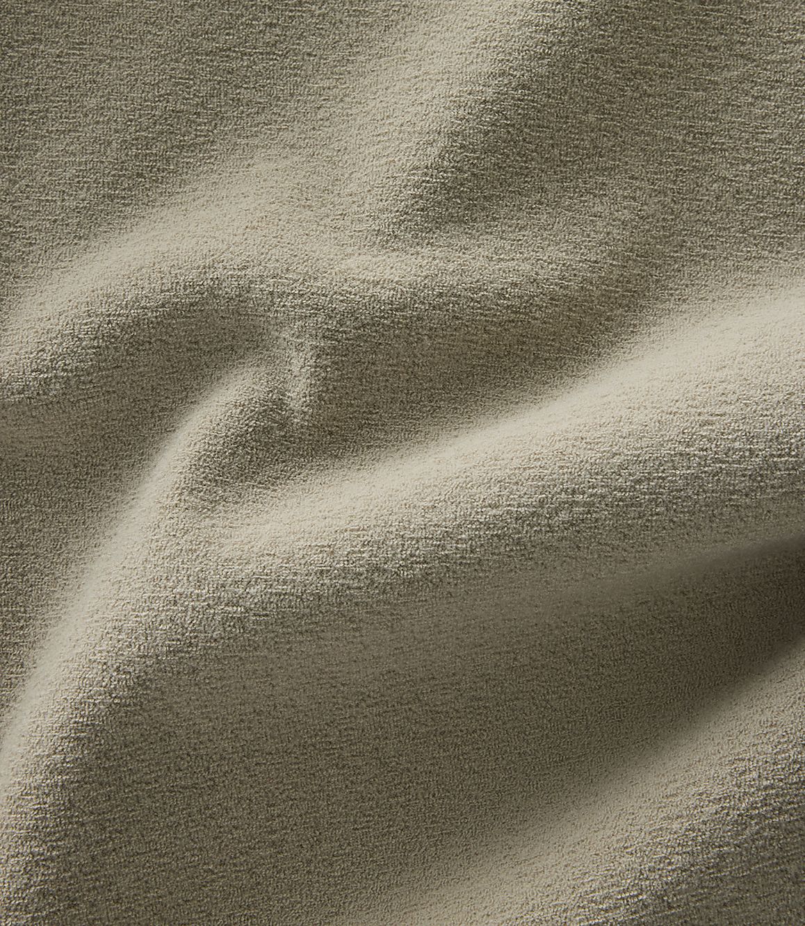 A close-up view of a textured, beige fabric with soft folds and shadows fills the frame.