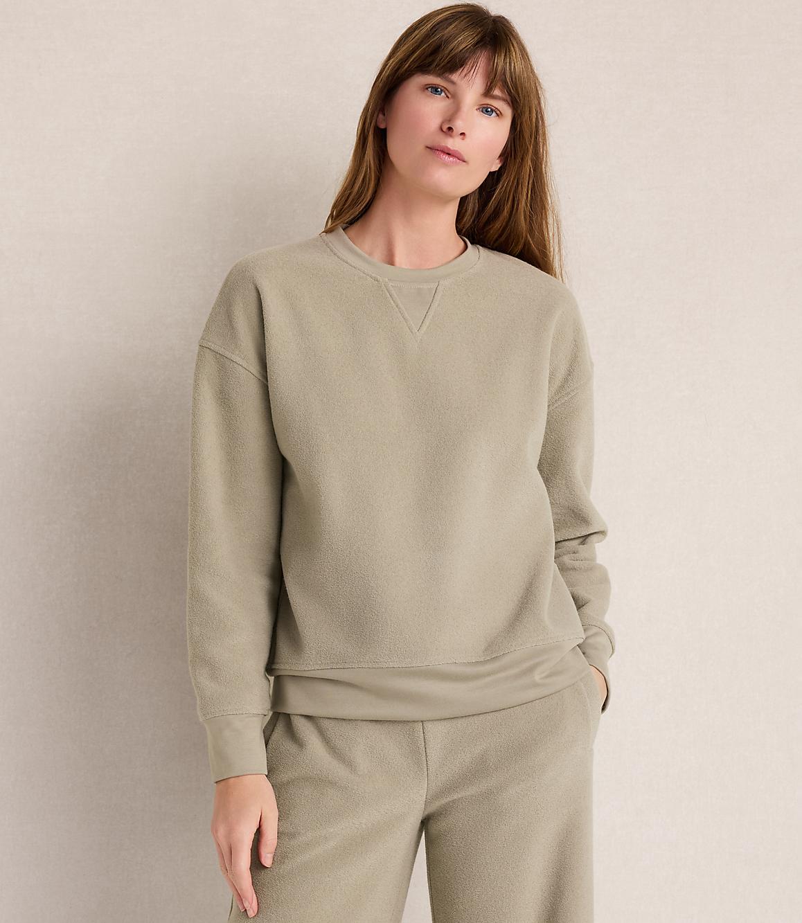 A woman in a light green sweatshirt and matching pants stands against a plain, light-colored background.
