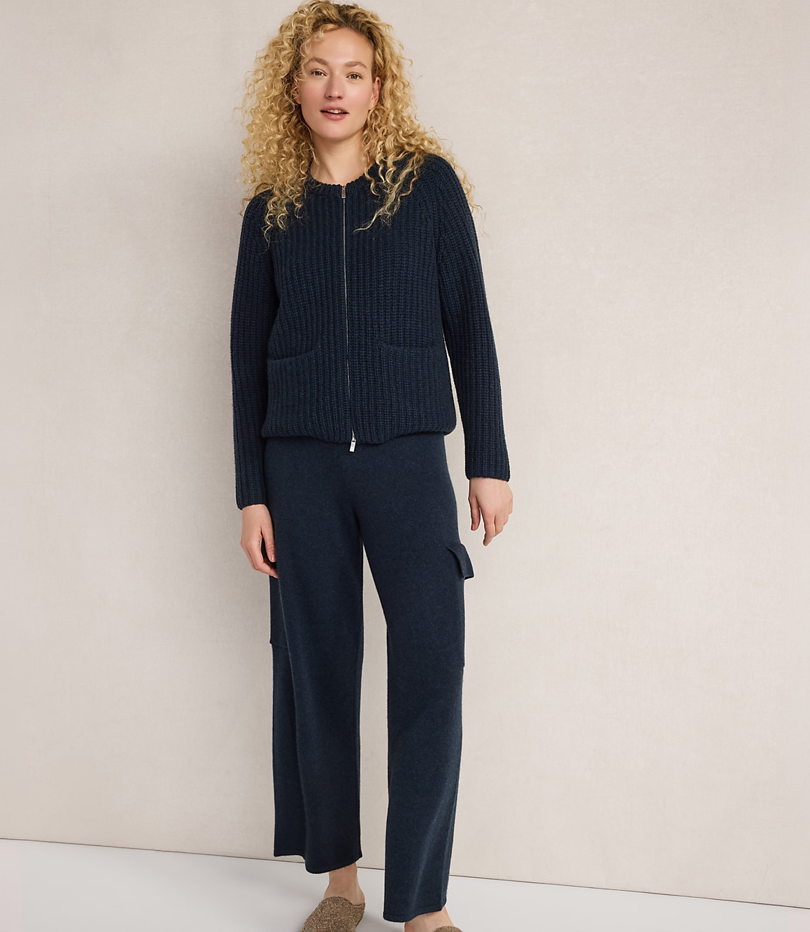 A woman in a navy blue ribbed cardigan and matching cargo pants stands against a plain, light-colored background.