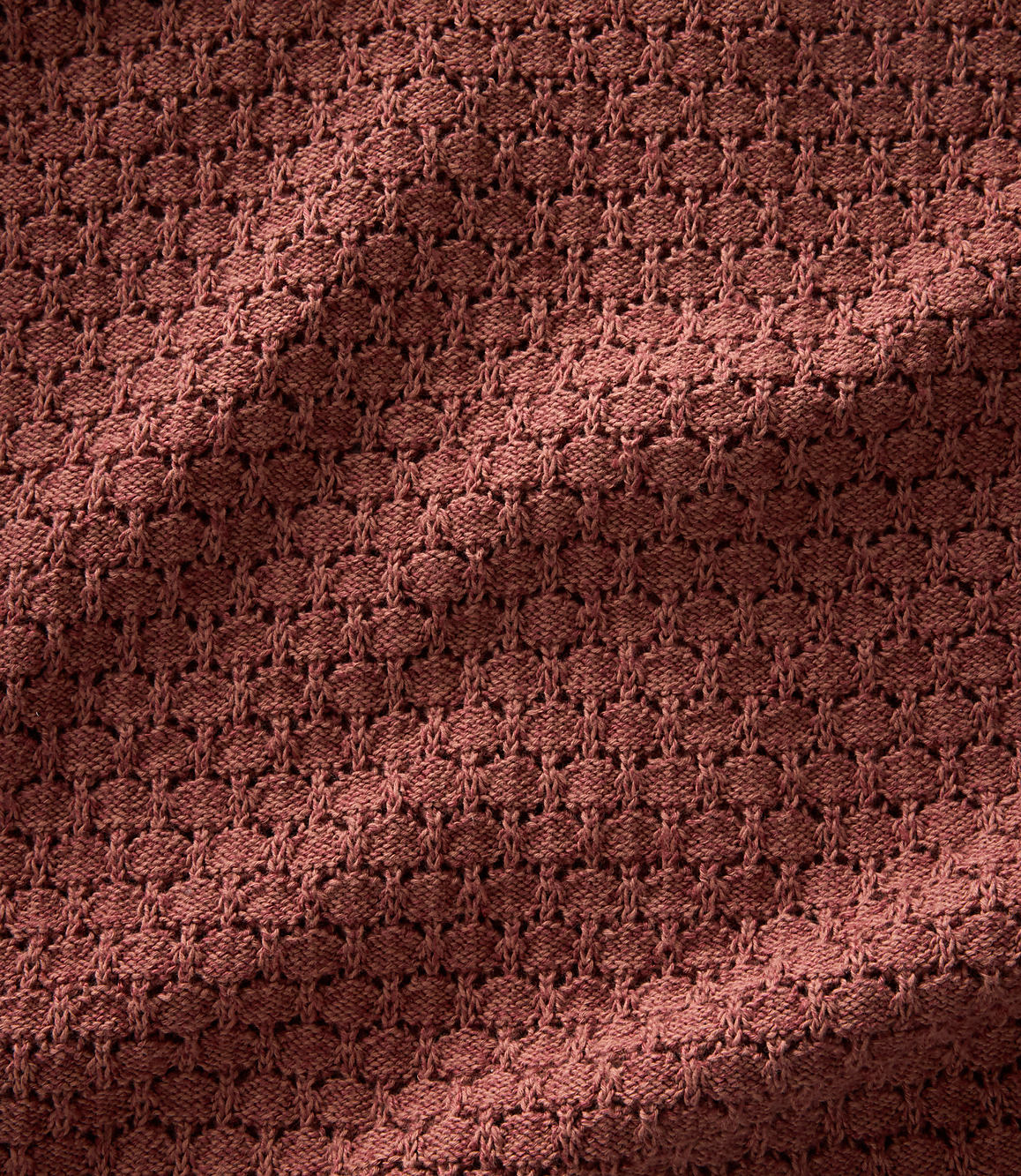A close-up view of a textured, reddish-brown knitted fabric with a subtle shadow cast across its surface.