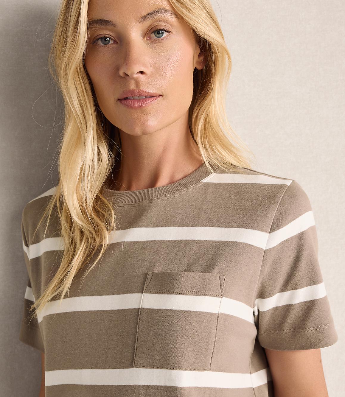 A blonde woman with a striped t-shirt and a pocket is in the foreground, with a plain, textured background behind her.