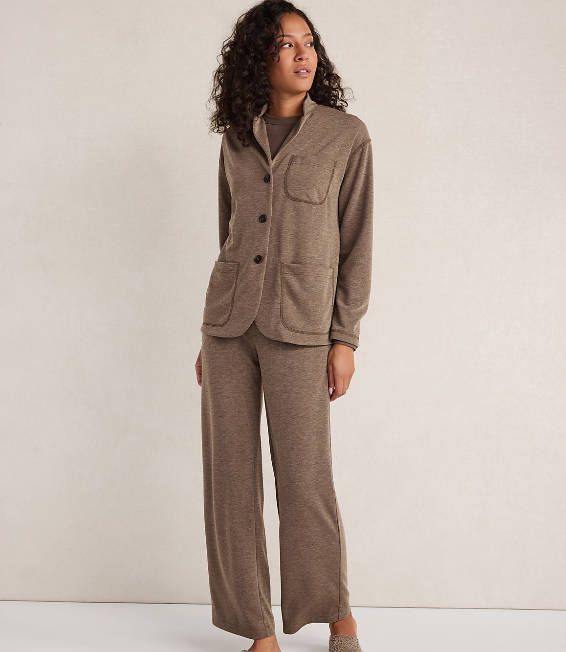 A woman in a brown loungewear set stands against a plain, light brown background.