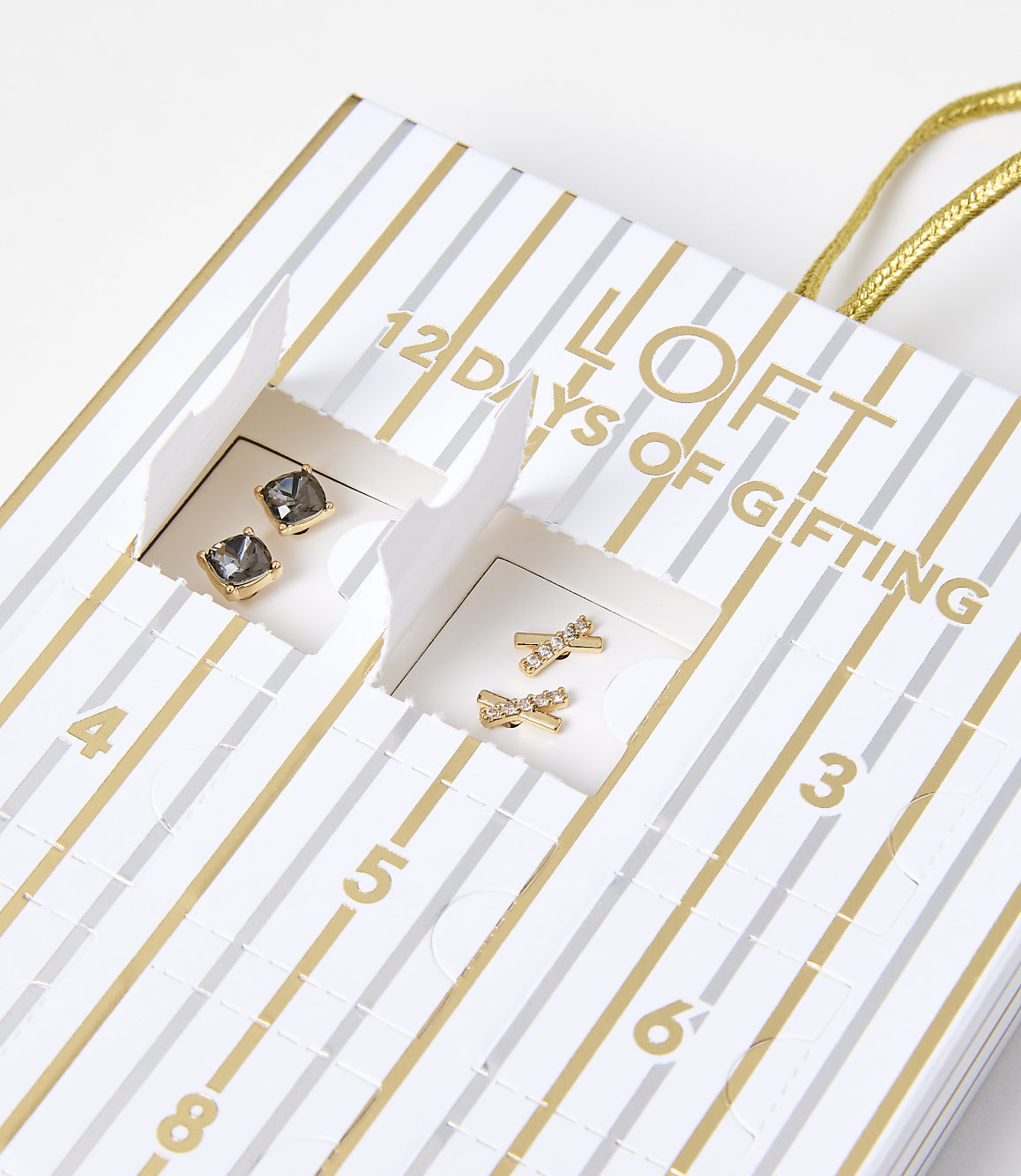 Two pairs of small, gold-toned earrings are visible in open compartments of a striped "12 Days of Gifting" advent calendar.