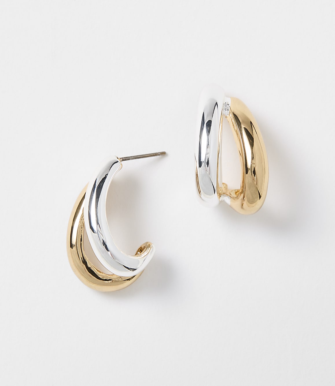 Two intertwined hoop earrings, one silver and one gold, rest on a plain white background.