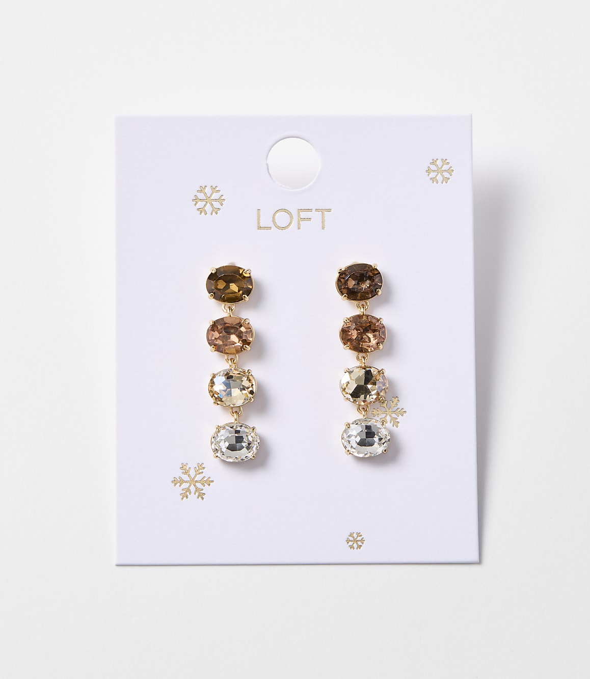 A pair of gold drop earrings with four oval-shaped gemstones in varying shades of brown and clear are displayed on a white card with snowflake accents and the "LOFT" logo.