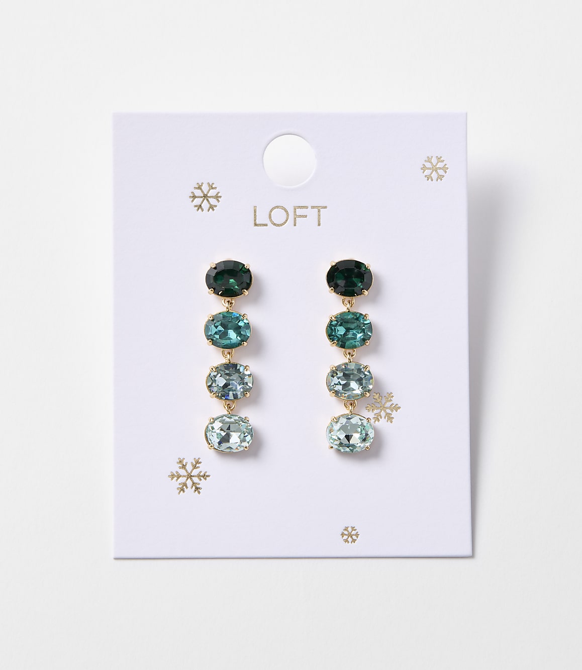 A pair of oval gemstone drop earrings in shades of green and blue hang from a white Loft card adorned with snowflakes.