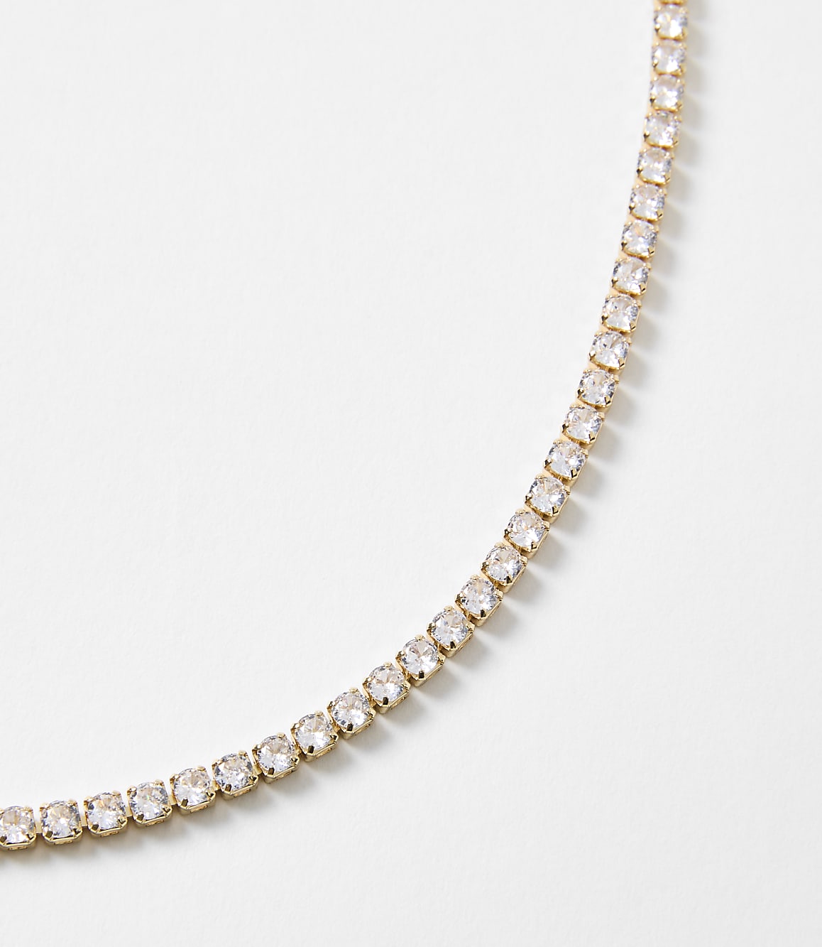 A delicate gold chain necklace with clear stones curves across a plain white background.