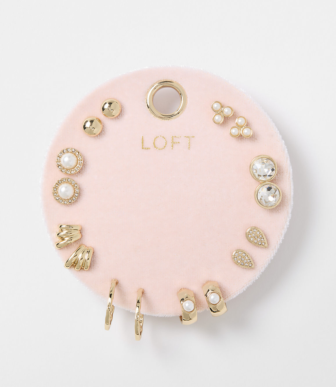 A collection of gold and pearl earrings are displayed on a pink velvet card against a white background.