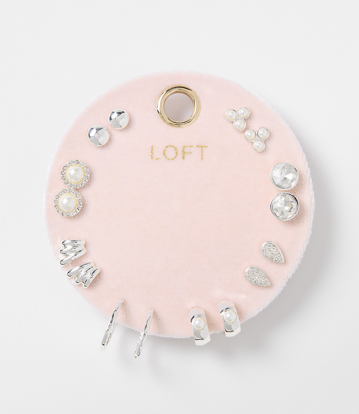 A collection of assorted silver and pearl earrings are displayed on a pink velvet circular backing with the "LOFT" logo, set against a plain white background.