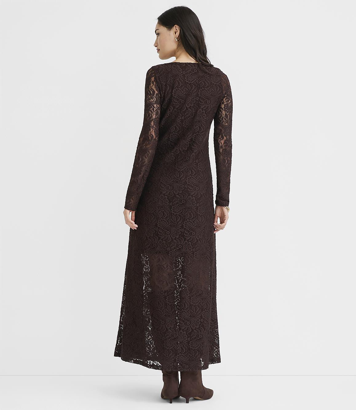 A woman in a long-sleeved brown lace dress stands against a plain white background.