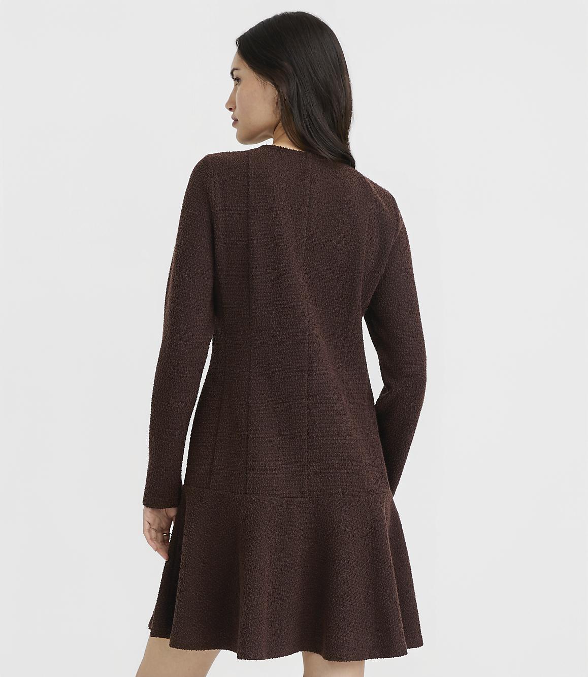 A woman in a brown textured dress stands against a plain white background.
