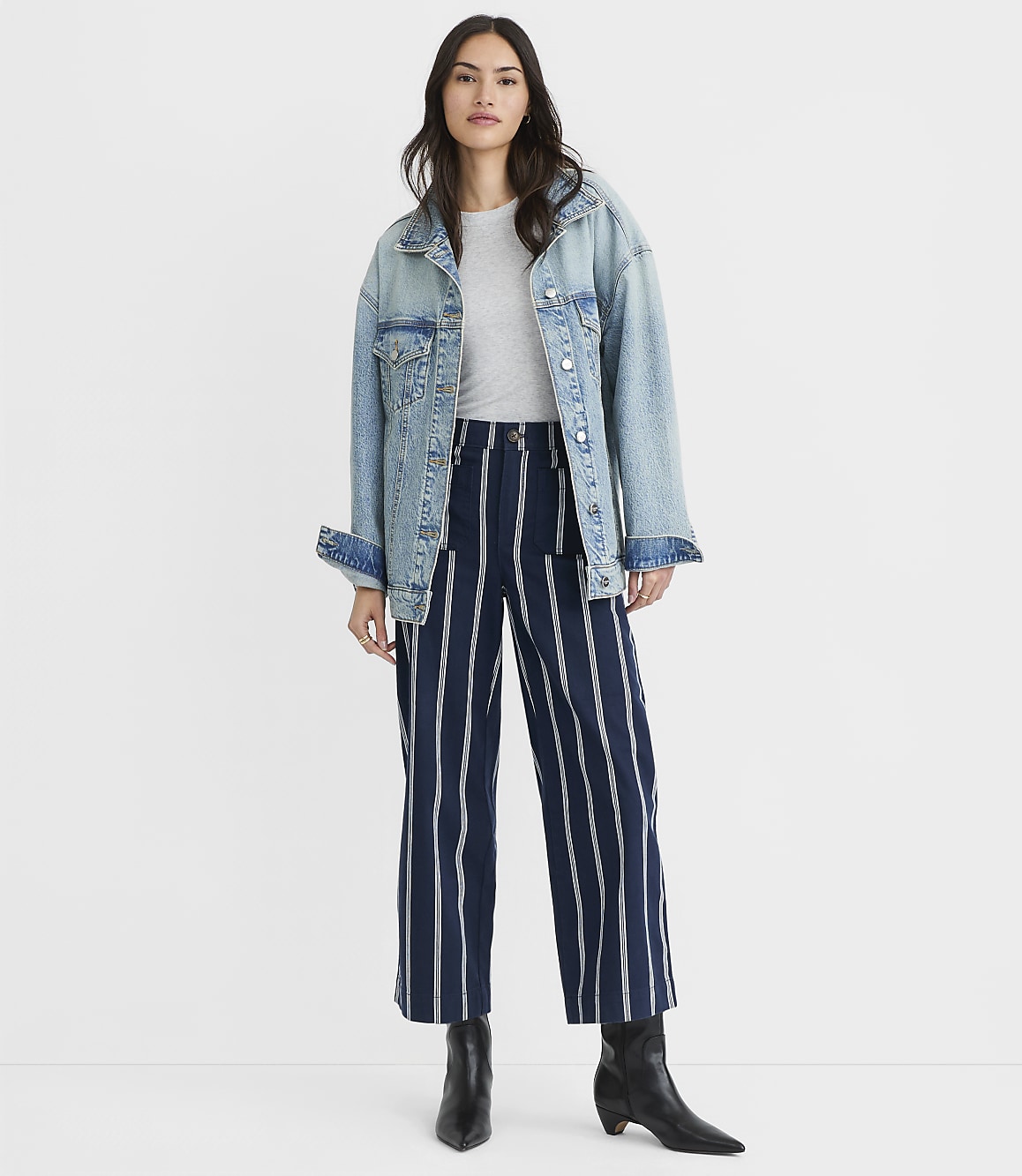 A woman in a denim jacket and striped pants stands against a plain white background.