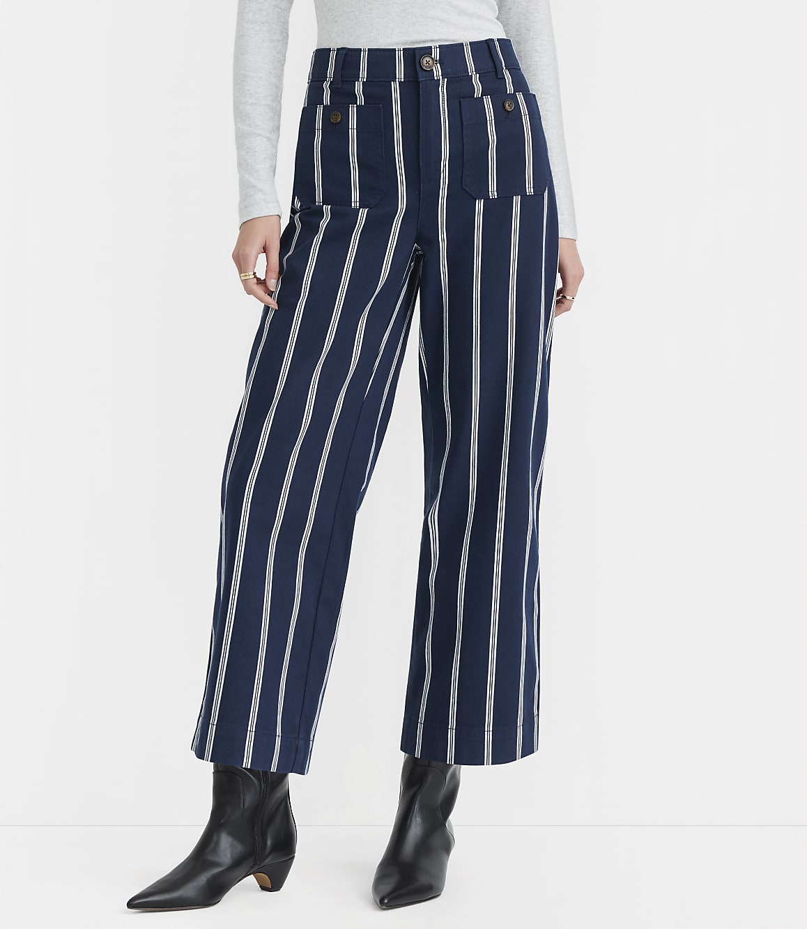 A person stands in front of a plain white background, wearing navy and white striped wide-leg pants and black boots.