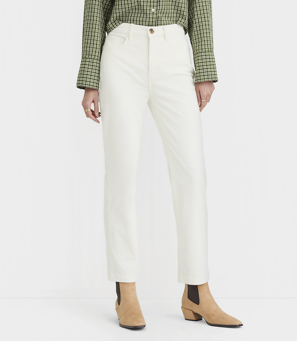 A person stands in white pants and a green checkered shirt, with tan boots, against a plain white background.