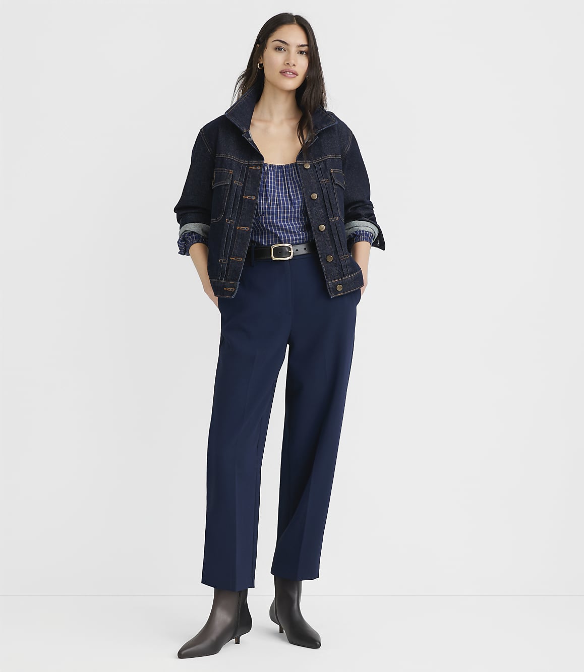 A woman in a denim jacket and blue pants stands against a plain white background.