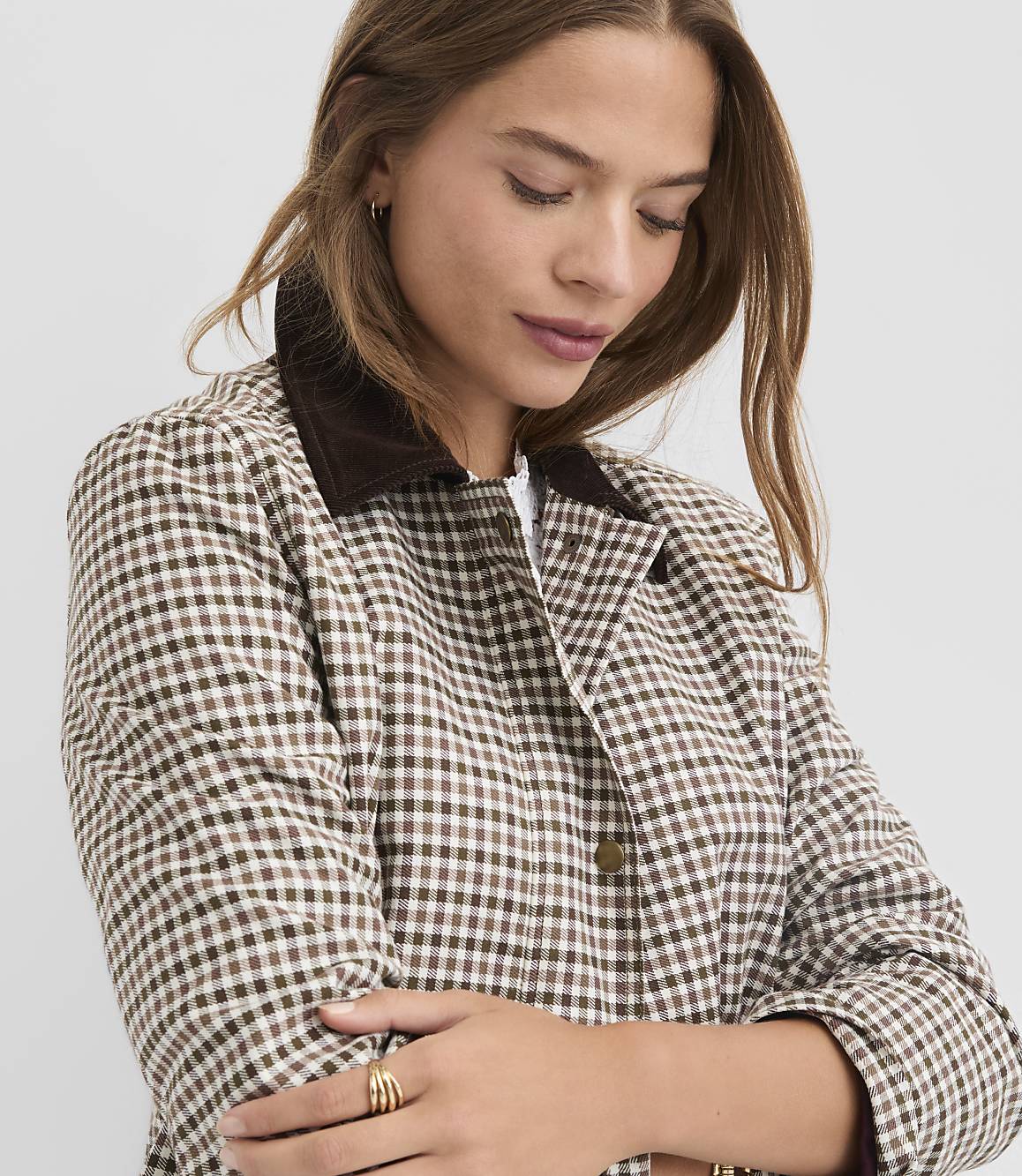 A woman in a brown and white gingham jacket with a corduroy collar poses against a plain gray background.