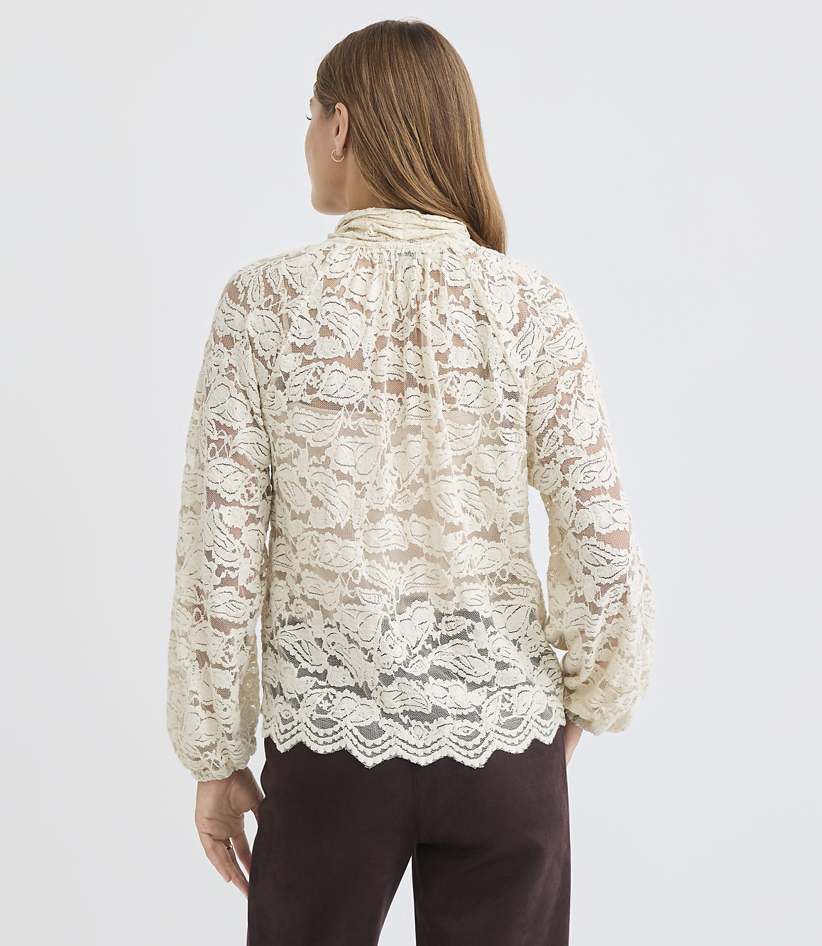 A woman in a cream lace blouse stands against a plain white background.