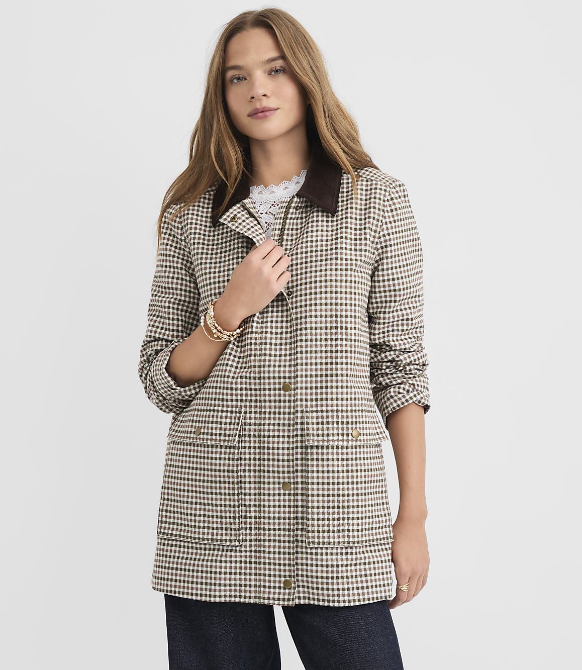 A woman in a checkered jacket stands against a plain, light gray background.
