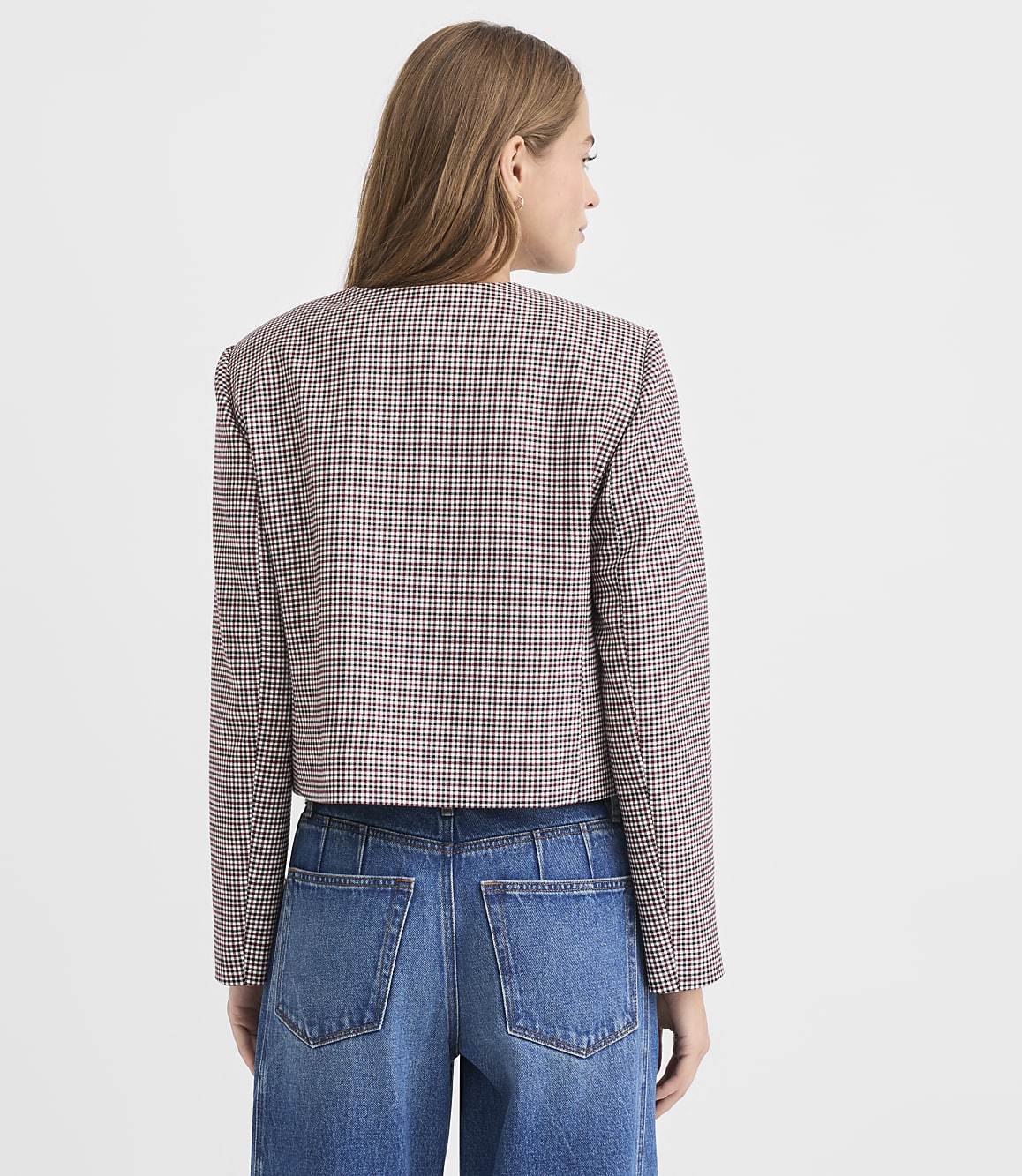 A woman in a patterned jacket and jeans stands against a plain white background.
