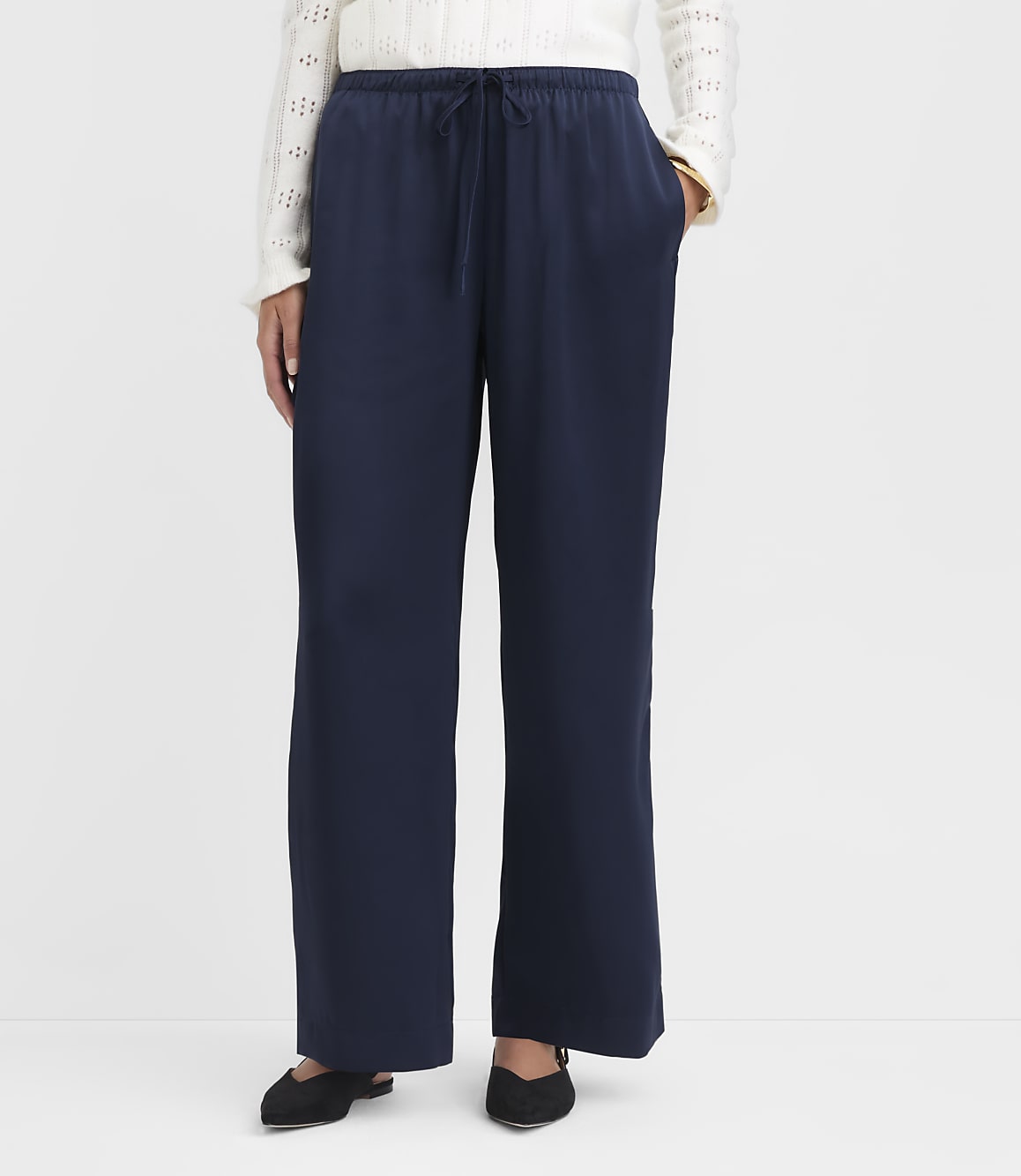 A person wearing navy blue wide-leg pants and a white sweater stands against a plain white background.