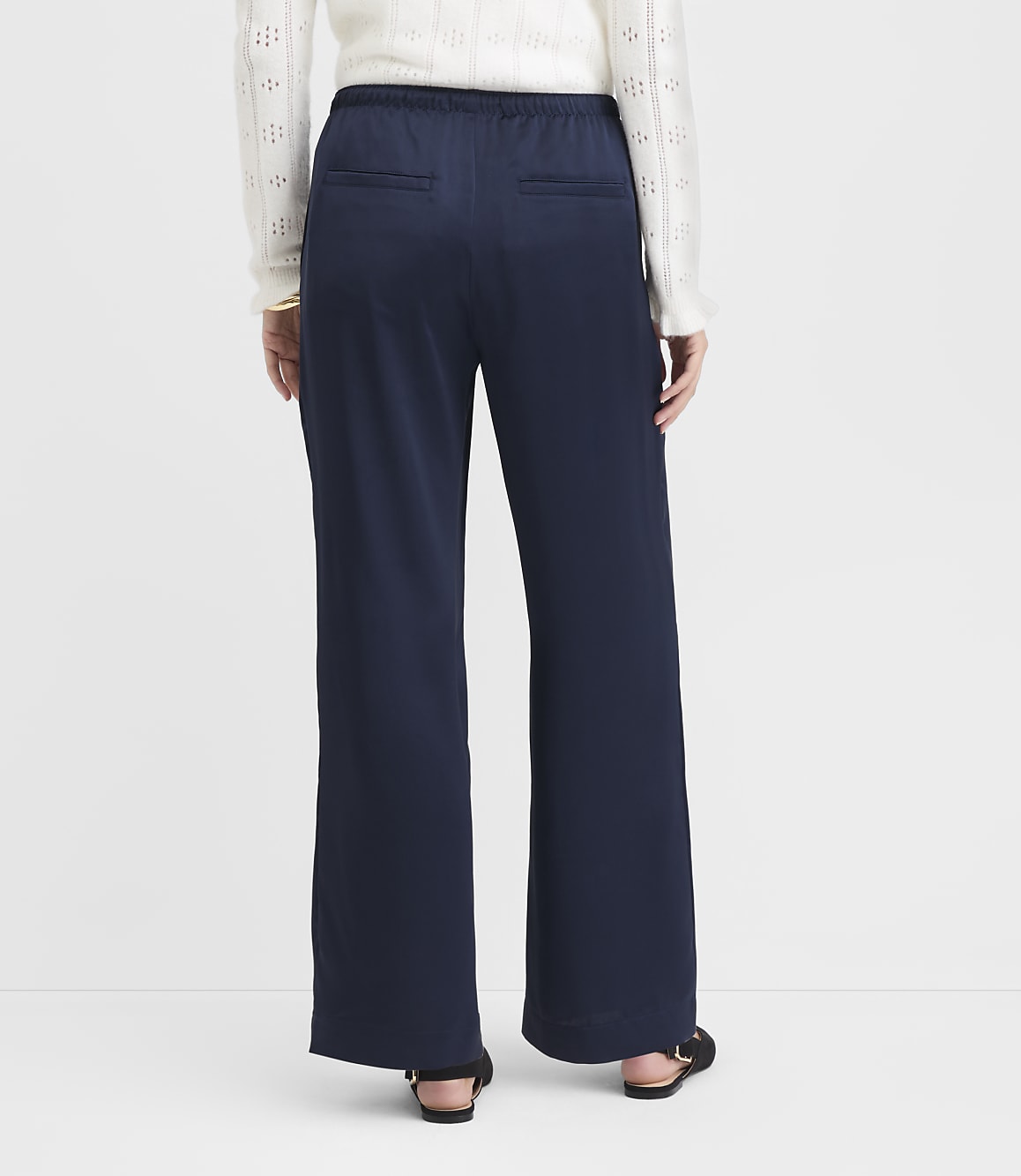 A person wearing navy wide-leg pants and a white sweater stands against a plain white background.