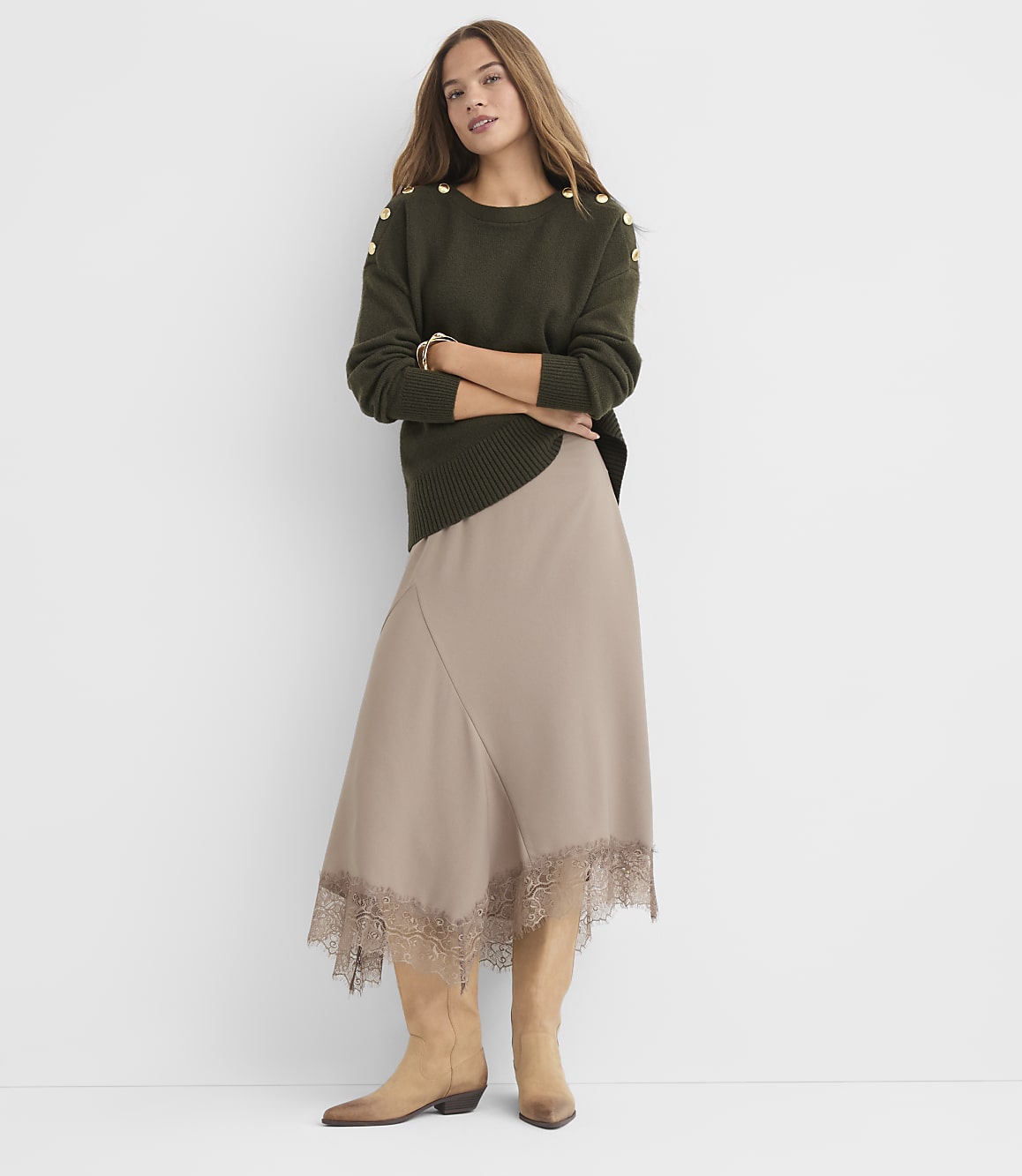 A woman in a green sweater and beige skirt stands against a plain white background.