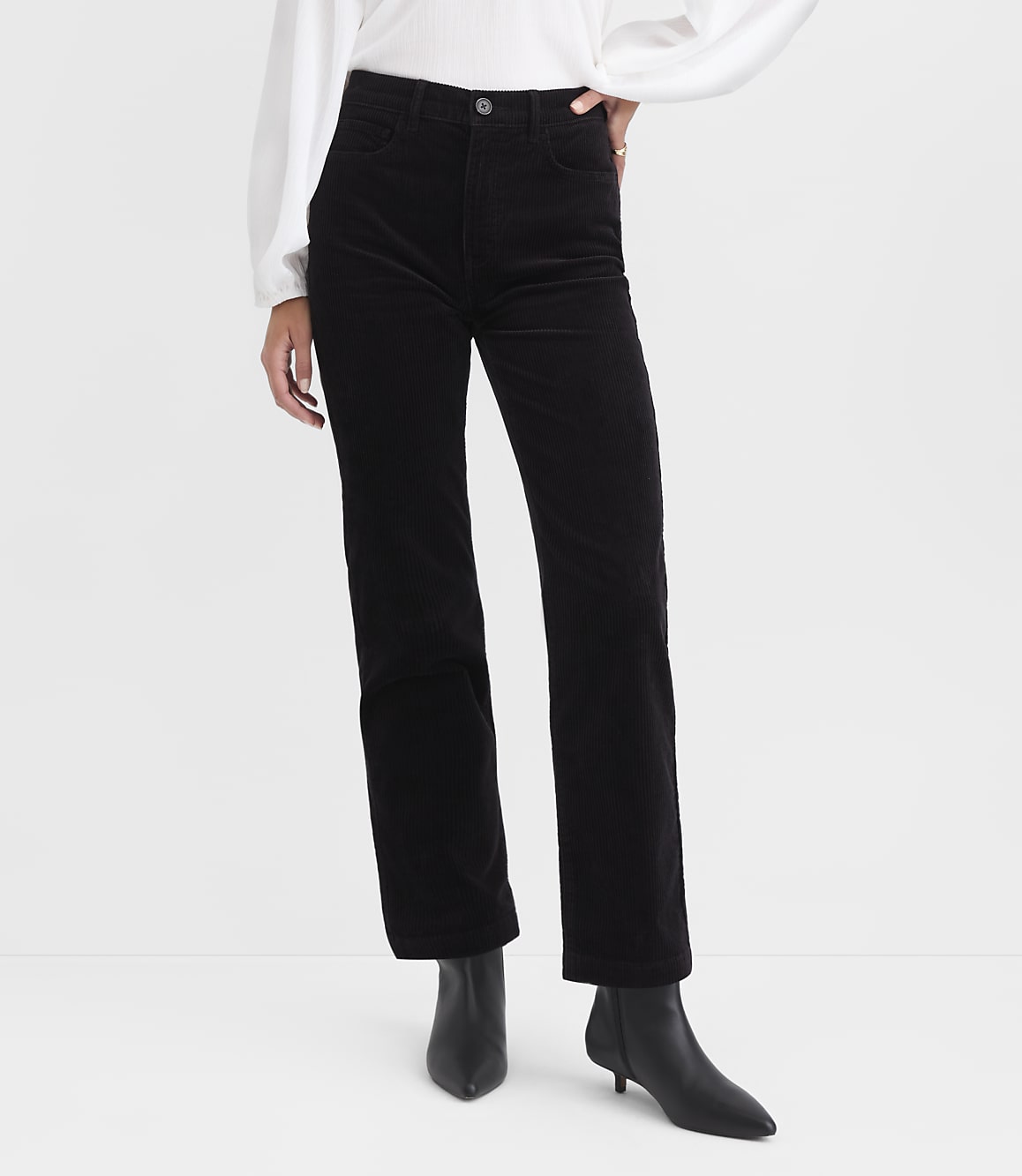 Black corduroy pants and black heeled boots are in the foreground, against a plain white background.