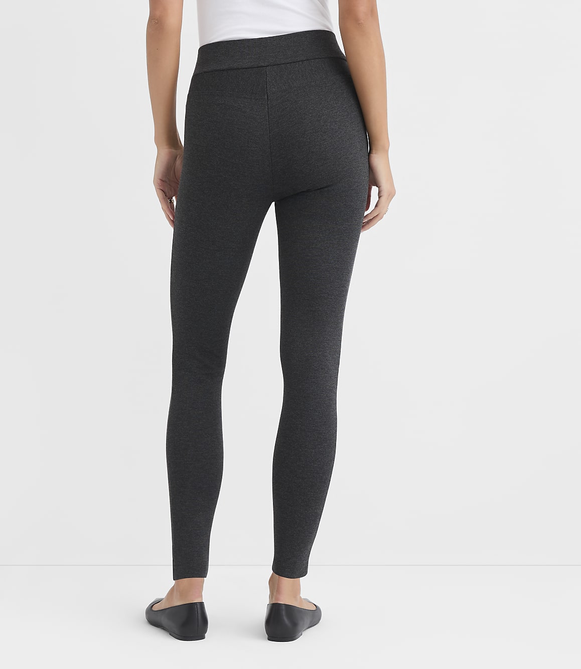 A person wearing dark grey patterned leggings and black ballet flats stands against a plain white background.