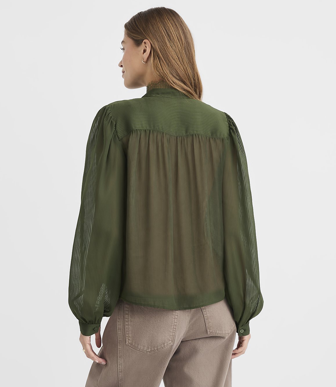 A woman in a green blouse stands against a plain white background.