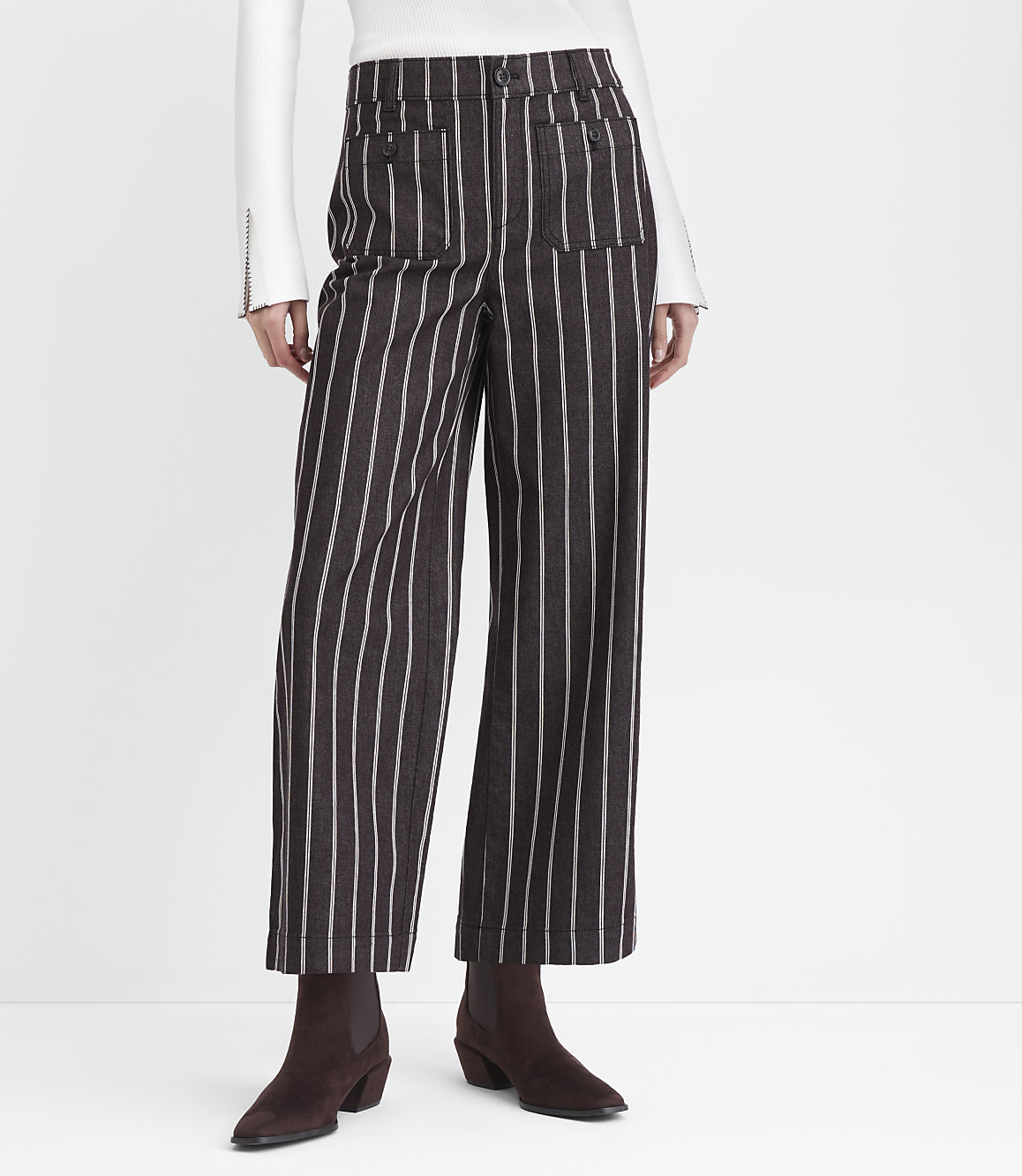 A person stands in front of a white background wearing brown and white striped wide-leg pants and dark brown boots.