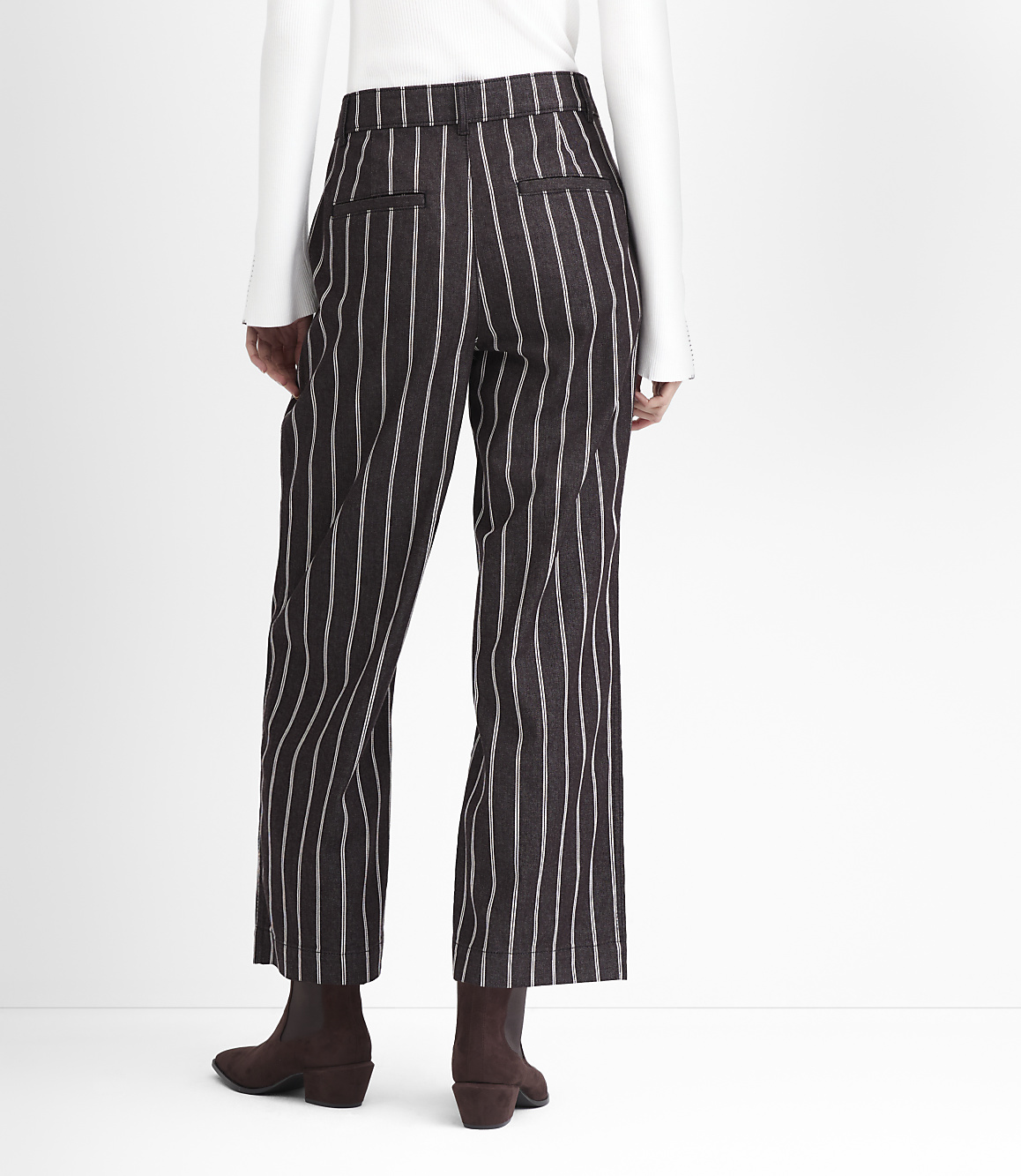 A person wearing pinstripe pants and brown boots stands against a plain white background.