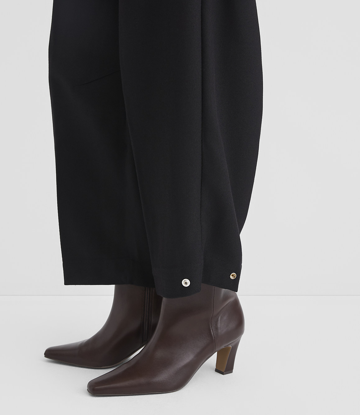 Black wide-leg trousers with silver button details are worn over brown leather ankle boots against a plain white background.