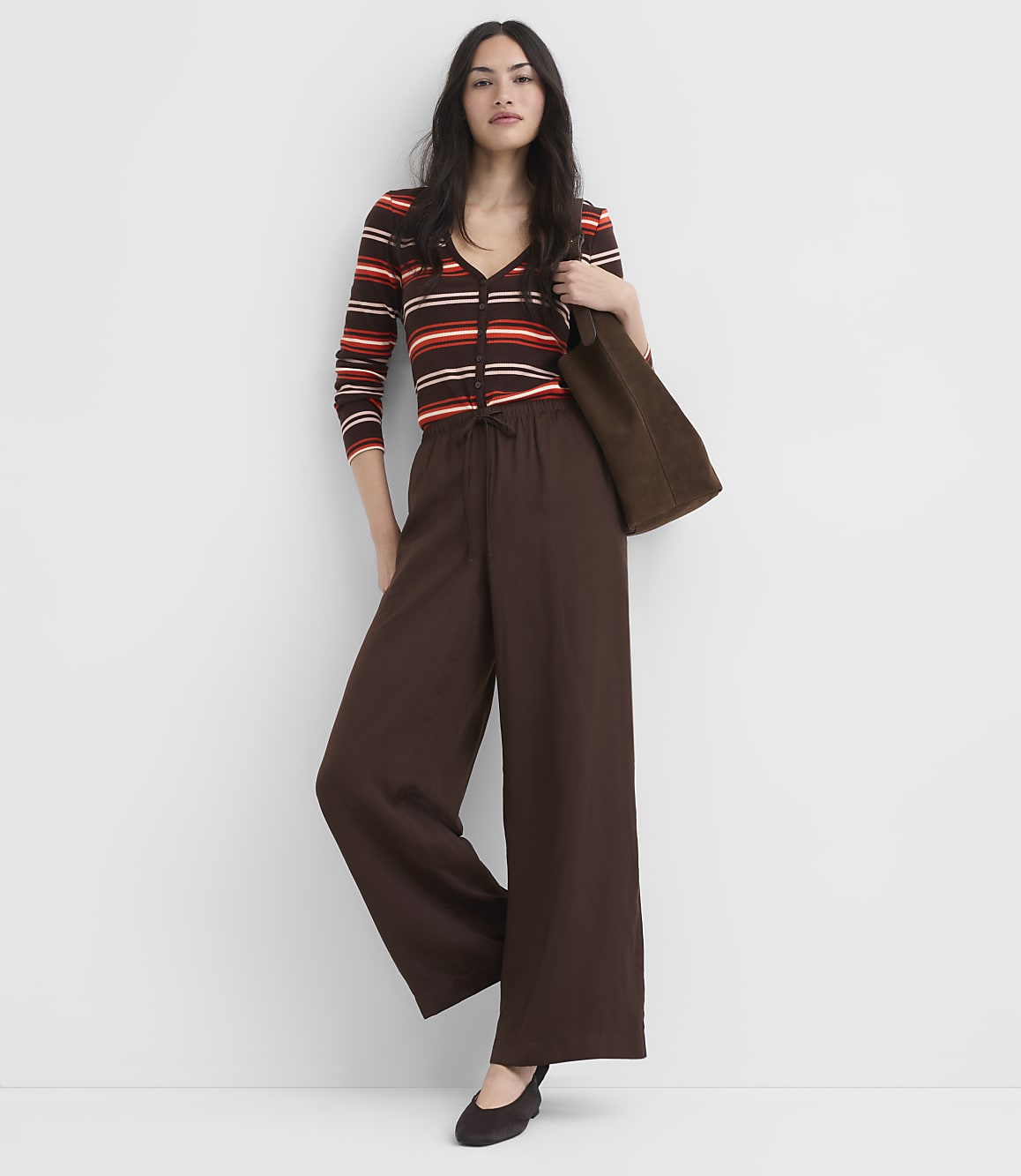 A woman in a striped top and wide-leg pants stands against a plain white background.