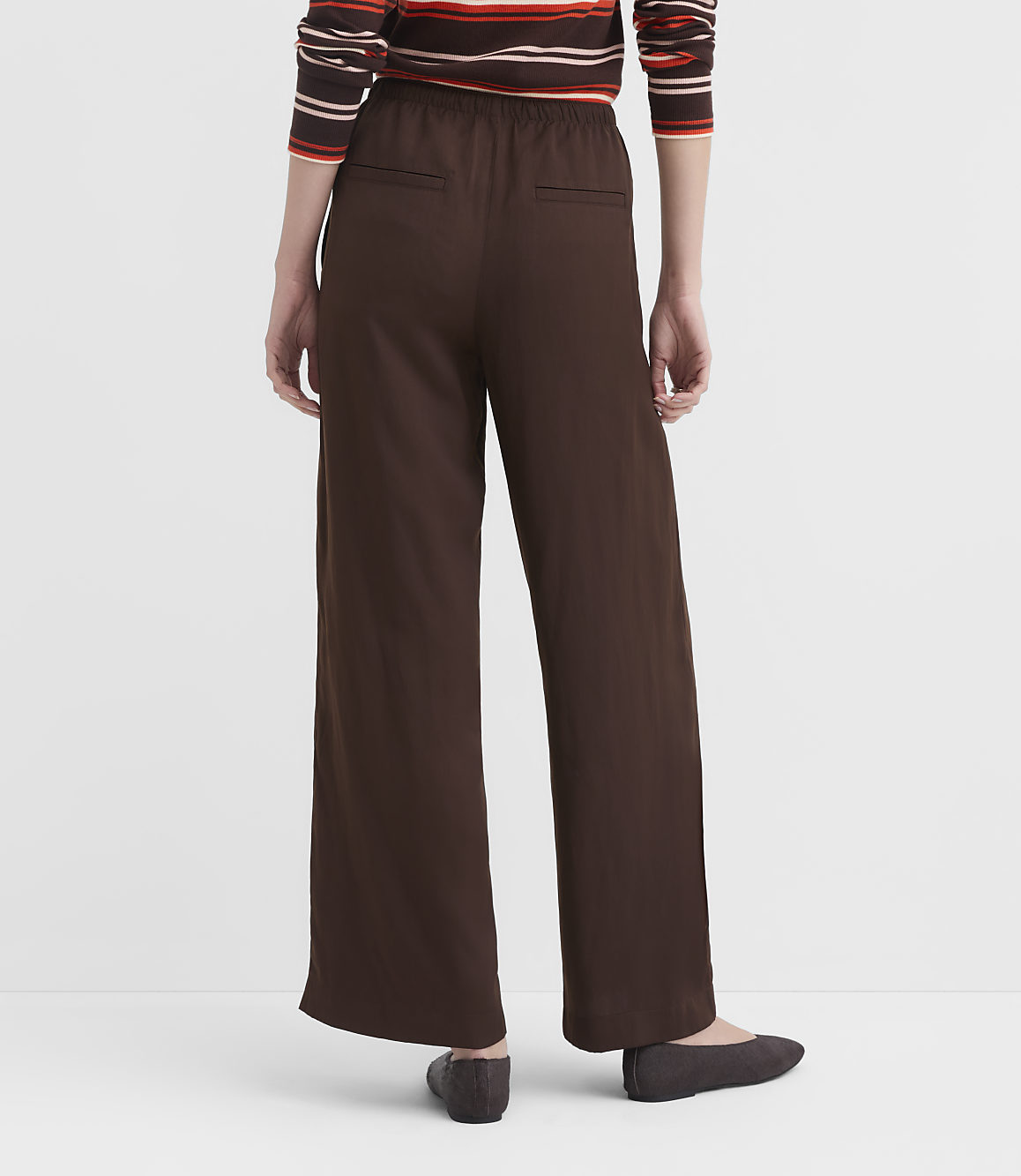 A person wearing brown wide-leg pants and a striped sweater stands against a plain white background.