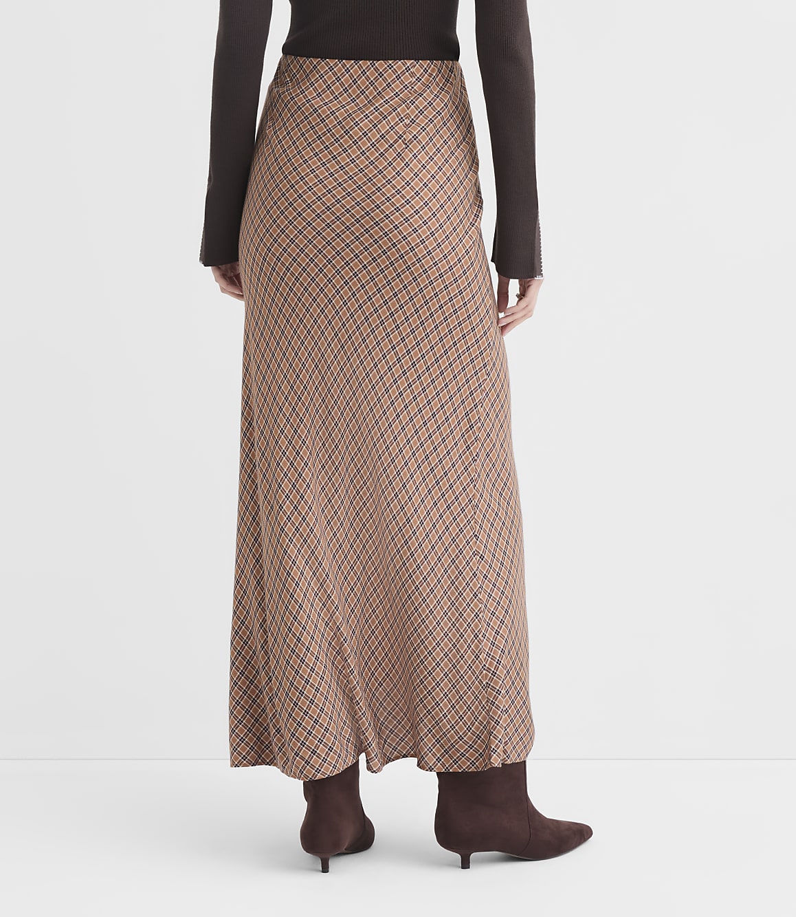 A person wearing a long, patterned skirt and brown boots stands against a plain white background.
